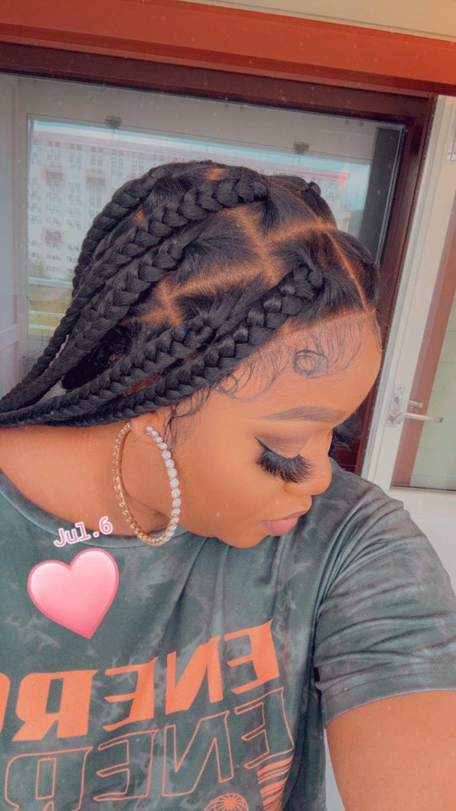 A person wearing a black braided wig with hair tied in a high ponytail, with visible braiding strands and a hair extension product advertisement in the background.